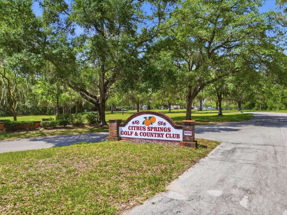 Brick entrance sign for the Citrus Springs Golf and Country Club under shady oak trees.